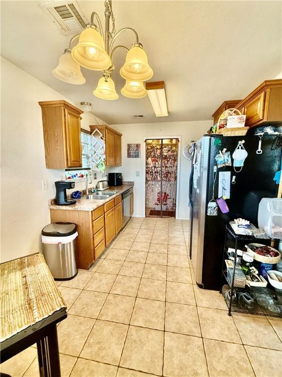 kitchen with light tile patterned floors, visible vents, brown cabinetry, stainless steel appliances, and a sink