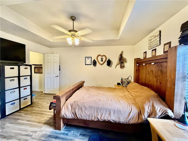 bedroom with a tray ceiling, light wood-style flooring, and ceiling fan
