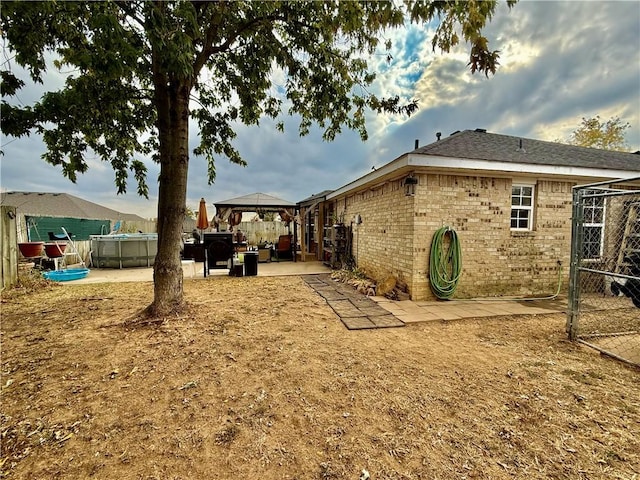 rear view of house with an outdoor pool, a gazebo, fence, a patio, and brick siding