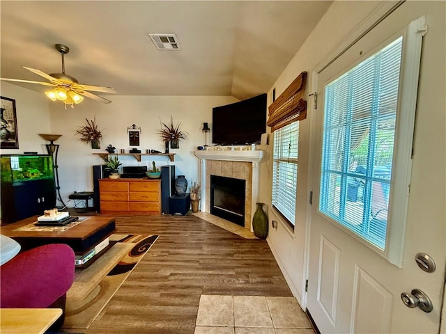 living room with visible vents, a ceiling fan, a tile fireplace, and lofted ceiling