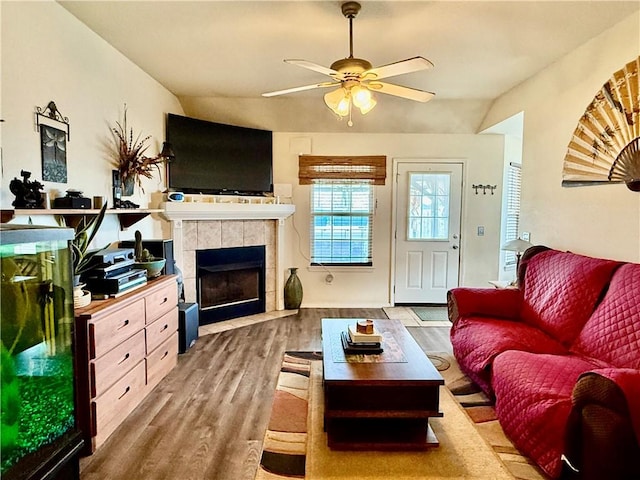living room with a tiled fireplace, ceiling fan, wood finished floors, and lofted ceiling