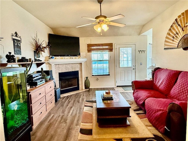 living area with light wood-style flooring, a ceiling fan, a tile fireplace, and lofted ceiling