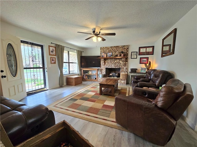 living room featuring a fireplace, a textured ceiling, a ceiling fan, and wood finished floors