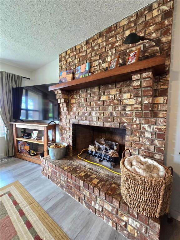 interior details featuring a textured ceiling, wood finished floors, and a brick fireplace