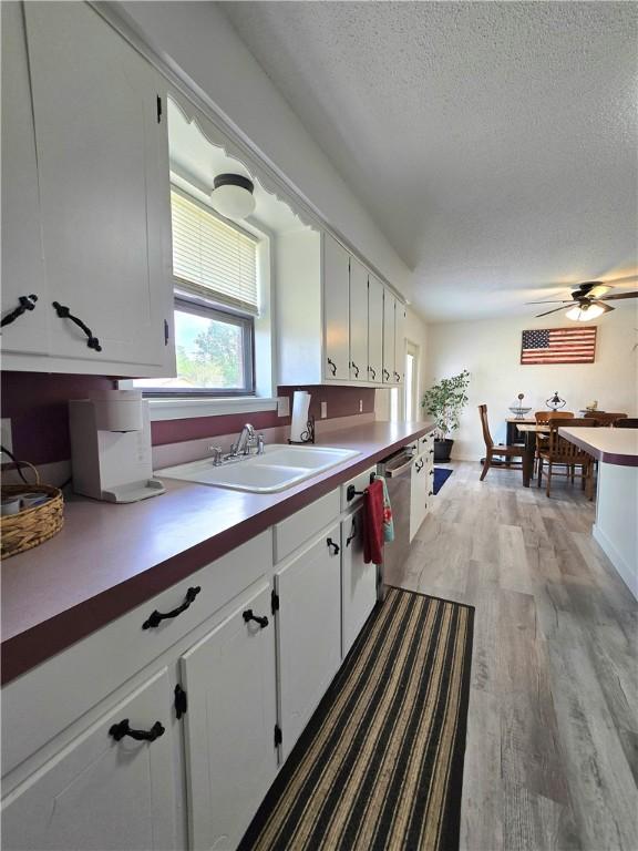 kitchen with dishwasher, a sink, a textured ceiling, light wood finished floors, and white cabinetry