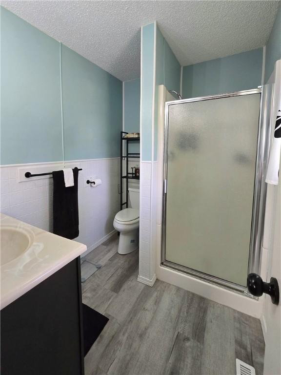 bathroom with tile walls, a textured ceiling, wood finished floors, a wainscoted wall, and a stall shower