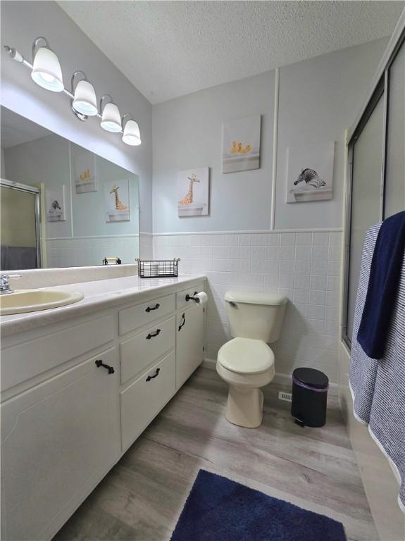 bathroom with vanity, a stall shower, a textured ceiling, toilet, and tile walls