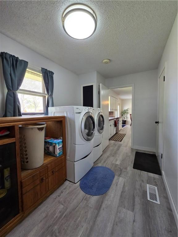laundry room with washing machine and dryer, a textured ceiling, visible vents, laundry area, and wood finished floors