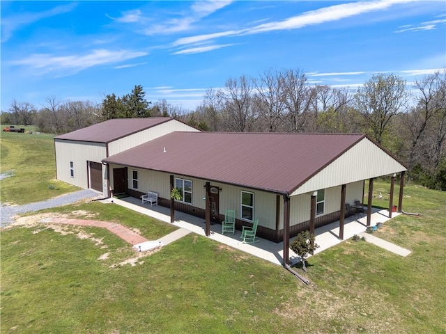 rear view of house featuring driveway, covered porch, metal roof, and a lawn