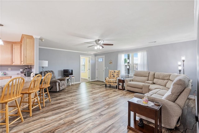 living room with crown molding, baseboards, light wood-type flooring, and a ceiling fan