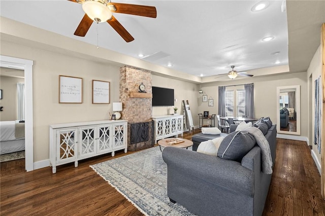living area featuring baseboards, ceiling fan, a tray ceiling, recessed lighting, and wood finished floors