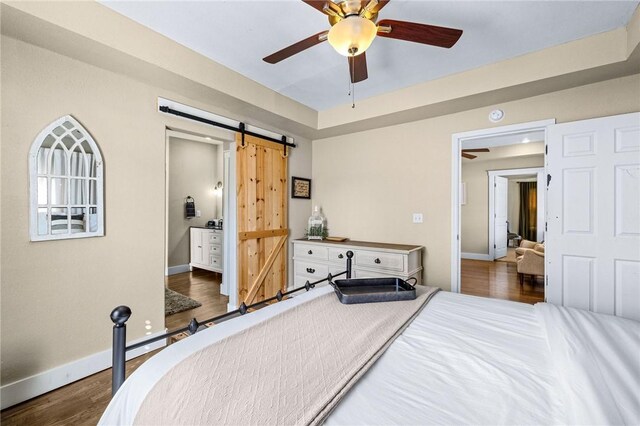 bedroom featuring ensuite bathroom, baseboards, a barn door, ceiling fan, and wood finished floors