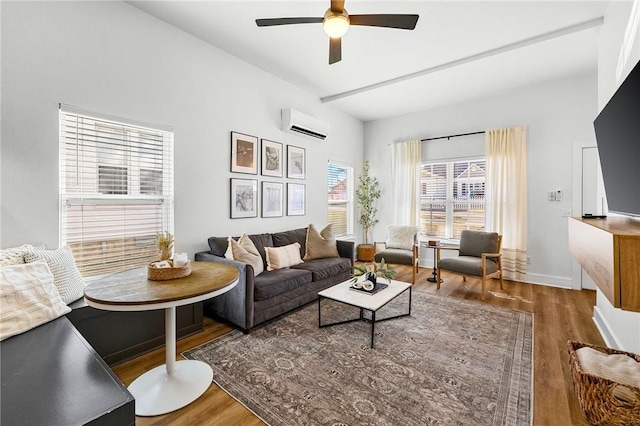 living area featuring wood finished floors, ceiling fan, baseboards, and a wall unit AC