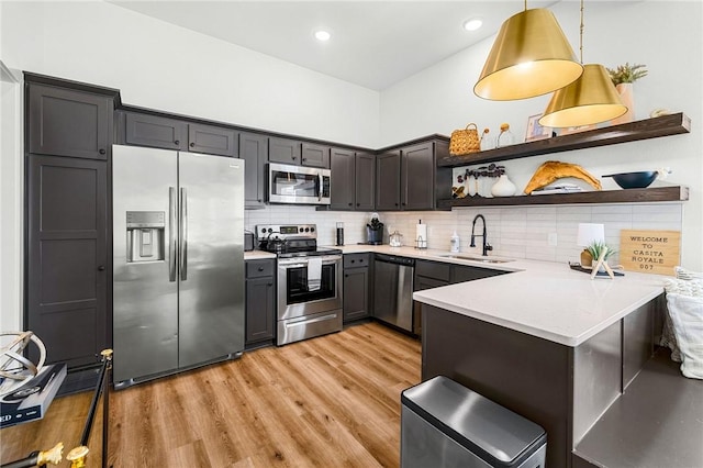 kitchen with light wood-type flooring, light countertops, open shelves, appliances with stainless steel finishes, and a sink