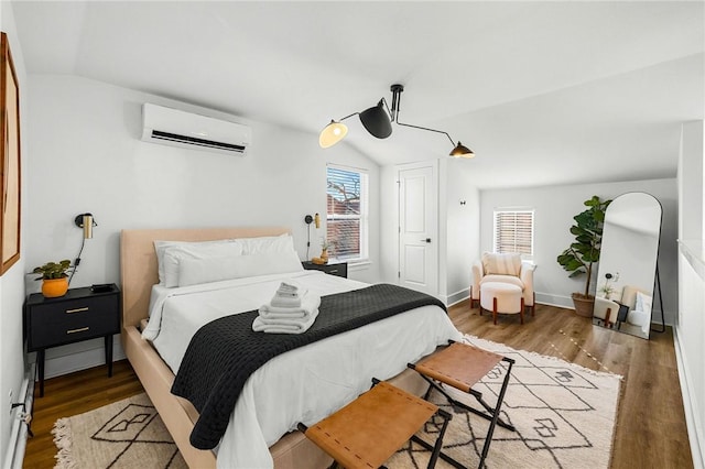 bedroom featuring a wall unit AC, wood finished floors, baseboards, and vaulted ceiling