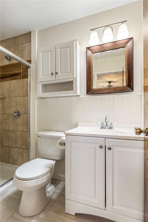 full bathroom featuring toilet, a stall shower, vanity, and wainscoting