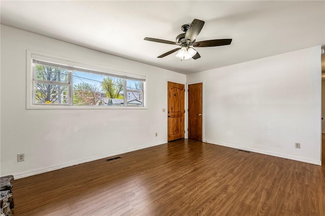 empty room featuring dark wood-type flooring, visible vents, baseboards, and a ceiling fan
