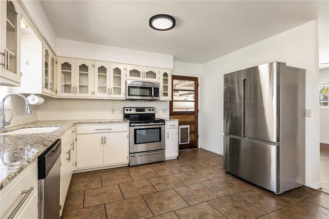 kitchen with glass insert cabinets, white cabinetry, appliances with stainless steel finishes, light stone counters, and a sink