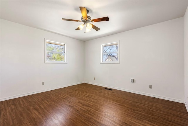 spare room with a healthy amount of sunlight, dark wood-style flooring, baseboards, and visible vents