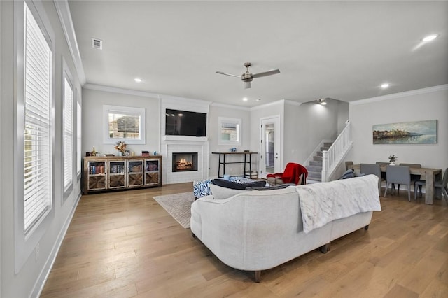 living room with ornamental molding, stairs, healthy amount of natural light, a fireplace, and light wood-style floors