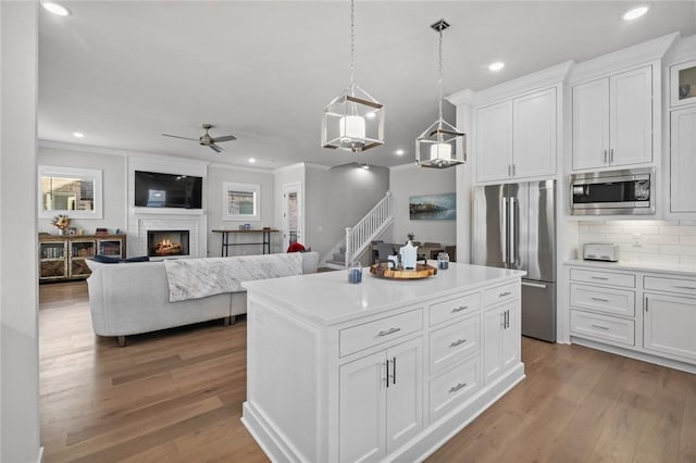 kitchen with stainless steel appliances, wood finished floors, ceiling fan, white cabinets, and crown molding