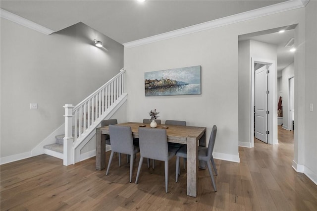 dining space featuring wood finished floors, stairs, crown molding, and baseboards