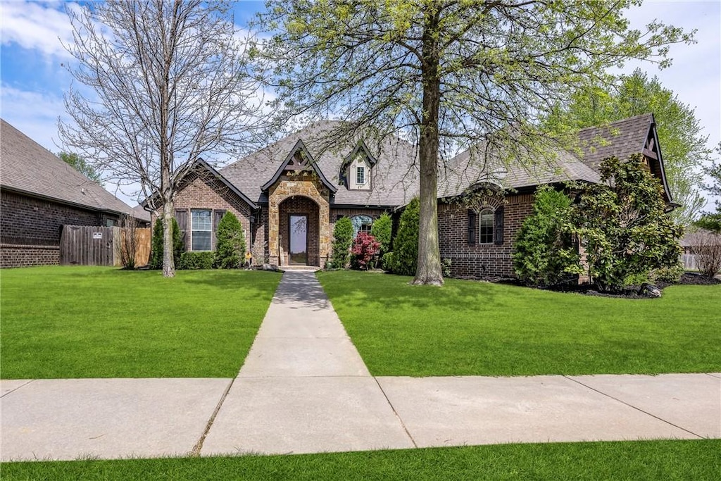 tudor house with a front yard, stone siding, fence, and brick siding