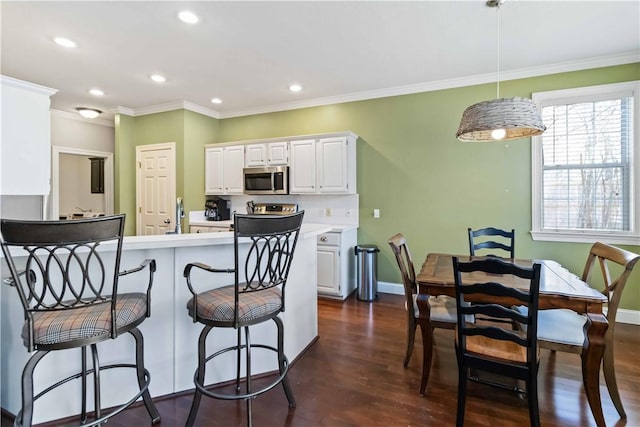 kitchen featuring dark wood-type flooring, white cabinetry, stainless steel microwave, light countertops, and a breakfast bar area