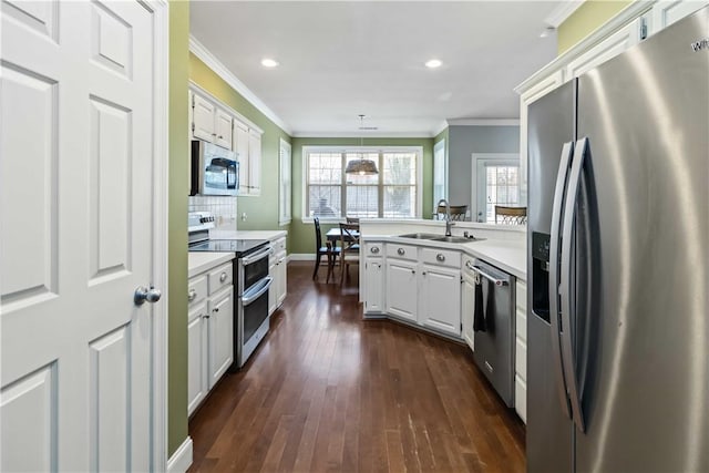 kitchen featuring crown molding, a peninsula, appliances with stainless steel finishes, a sink, and light countertops