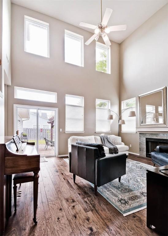 living room featuring a high ceiling, a fireplace, ceiling fan, baseboards, and wood finished floors