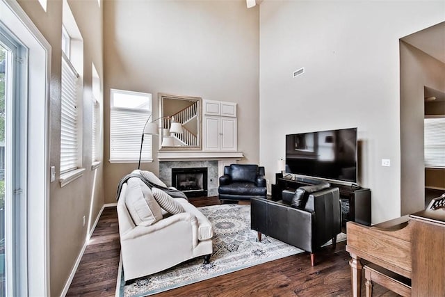 living area featuring dark wood finished floors, a fireplace, baseboards, visible vents, and a high ceiling