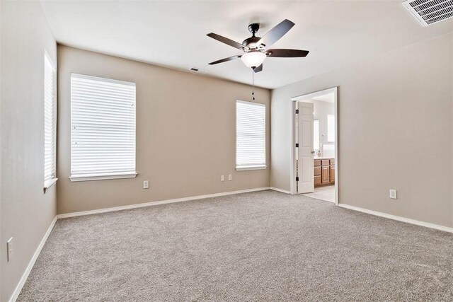 interior space featuring baseboards, visible vents, ceiling fan, and light colored carpet