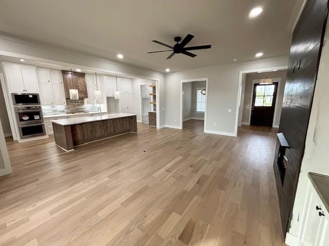 7919 Via Roma Ave, Springdale, AR 72762 - kitchen featuring open floor plan, appliances with stainless steel finishes, backsplash, white cabinetry, and light wood-style flooring