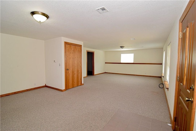 basement featuring baseboards, light colored carpet, a textured ceiling, and visible vents