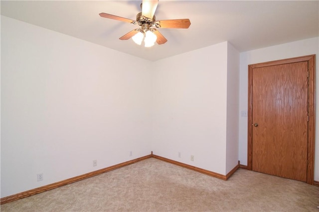 empty room featuring baseboards, a ceiling fan, and light carpet