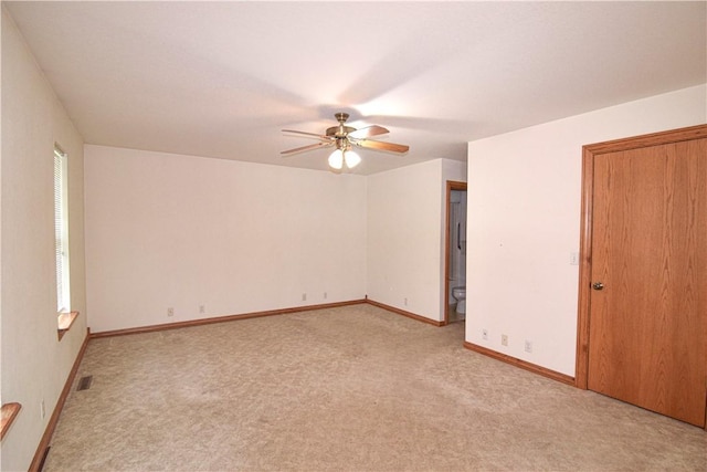spare room with a ceiling fan, baseboards, visible vents, and light carpet