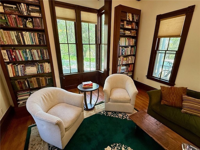 sitting room with baseboards, wall of books, built in features, and wood finished floors