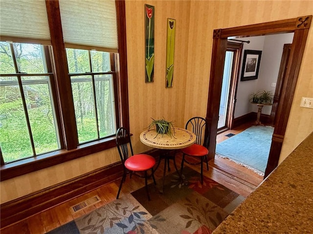 dining area with a healthy amount of sunlight, wallpapered walls, visible vents, and wood finished floors