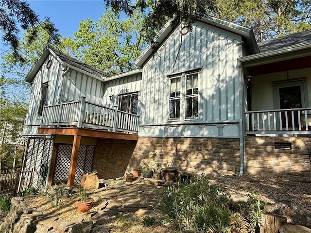 rear view of property featuring board and batten siding, roof with shingles, and a deck