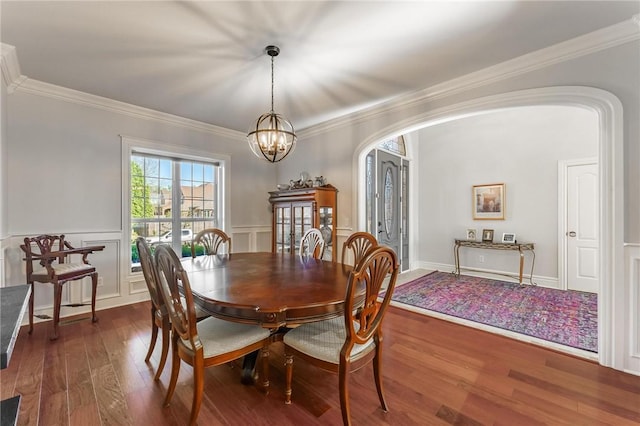 dining room featuring arched walkways, a decorative wall, crown molding, a chandelier, and dark wood-style flooring