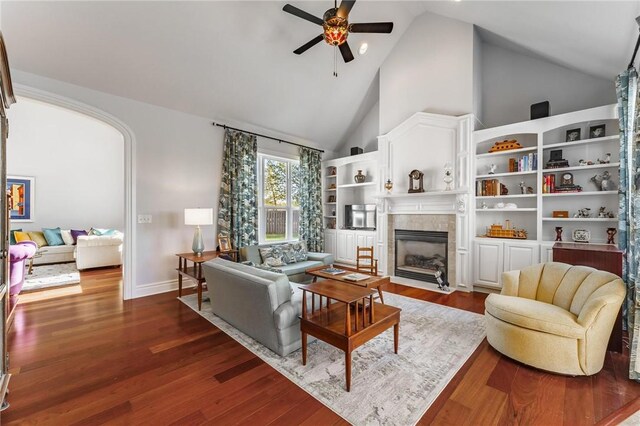 living area with high vaulted ceiling, a ceiling fan, a tile fireplace, baseboards, and dark wood-type flooring