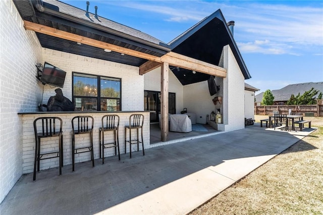 exterior space with brick siding, outdoor dry bar, a patio area, and fence