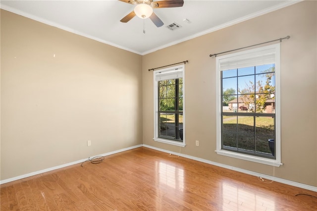 empty room featuring wood finished floors, visible vents, crown molding, and a wealth of natural light