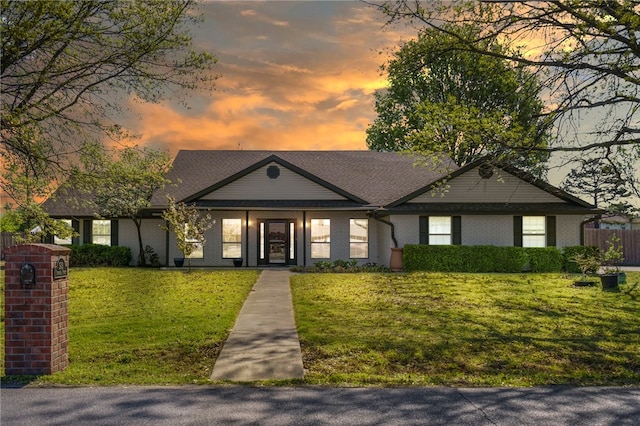 view of front of property with brick siding, a yard, and fence