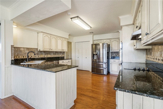 kitchen with under cabinet range hood, stainless steel appliances, backsplash, a peninsula, and ornamental molding
