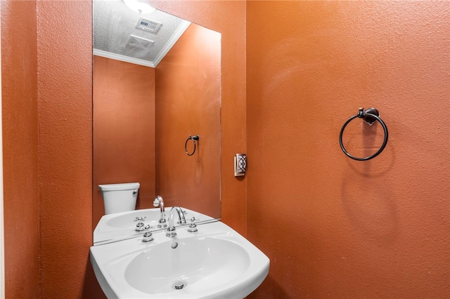 half bathroom featuring a textured wall, visible vents, crown molding, and a sink