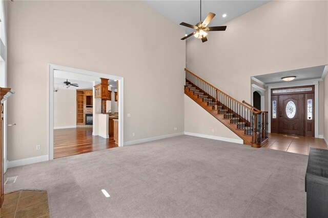 3902 NE Cadbury Ave, Bentonville, AR 72712 - unfurnished living room featuring ceiling fan, stairway, a towering ceiling, carpet, and baseboards