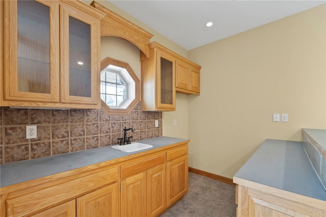 3902 NE Cadbury Ave, Bentonville, AR 72712 - kitchen featuring a sink, decorative backsplash, glass insert cabinets, baseboards, and light countertops