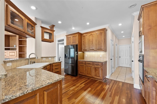3902 NE Cadbury Ave, Bentonville, AR 72712 - kitchen with stainless steel appliances, brown cabinetry, a sink, light stone countertops, and glass insert cabinets
