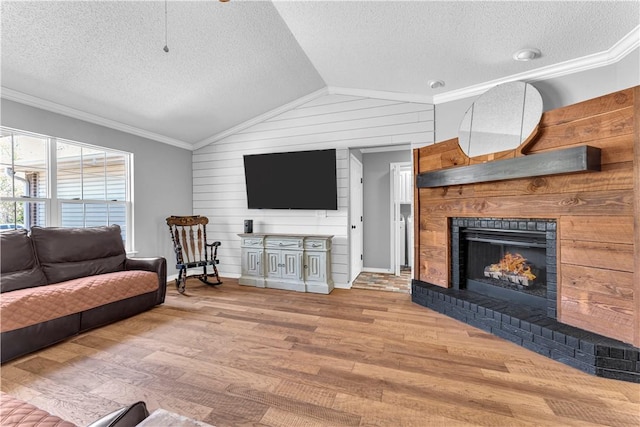 living room featuring ornamental molding, a textured ceiling, lofted ceiling, wood finished floors, and a brick fireplace
